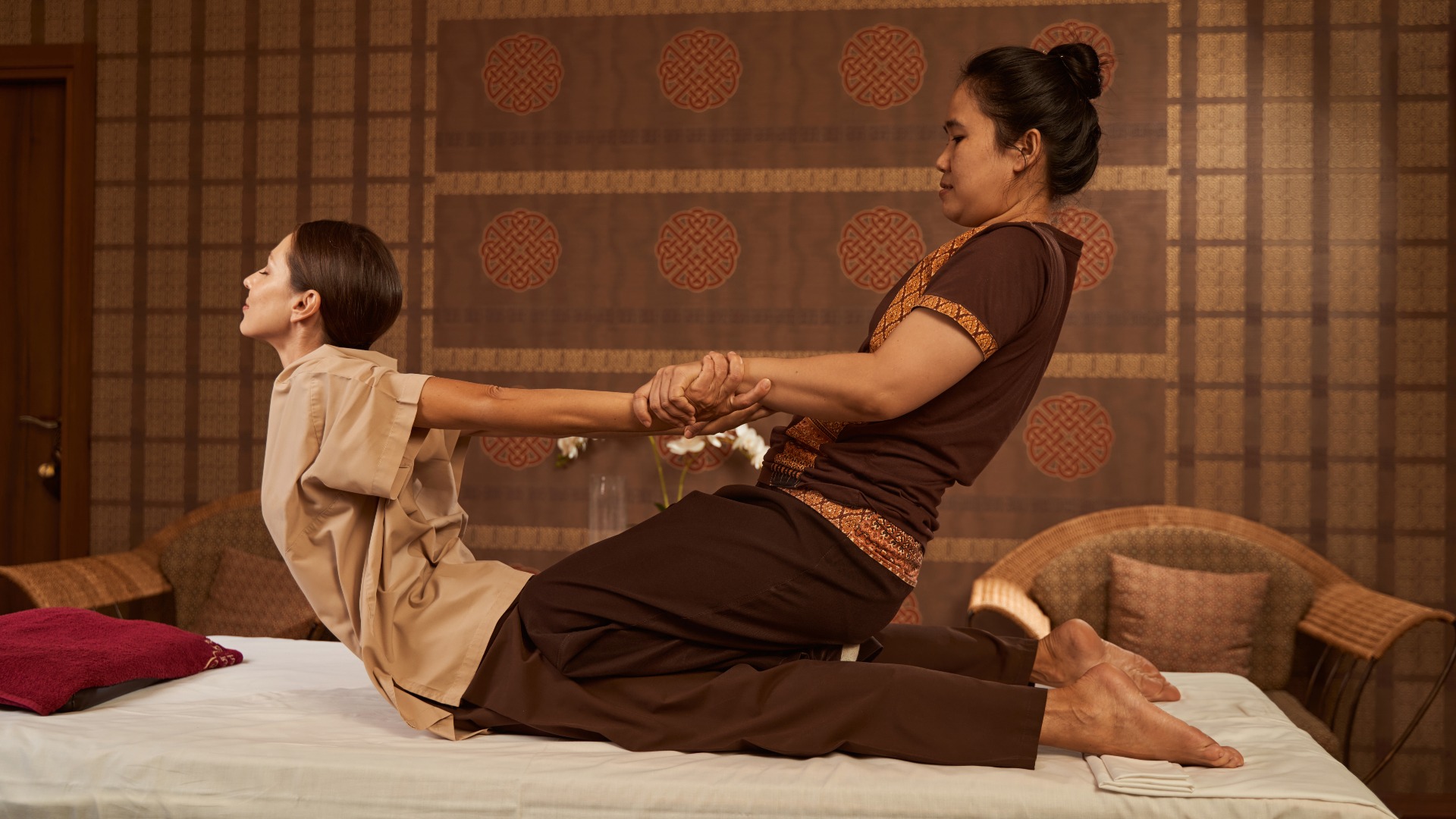 Therapeutin dehnt die Rückenmuskulatur ihrer Klientin bei einer Thai-Massage